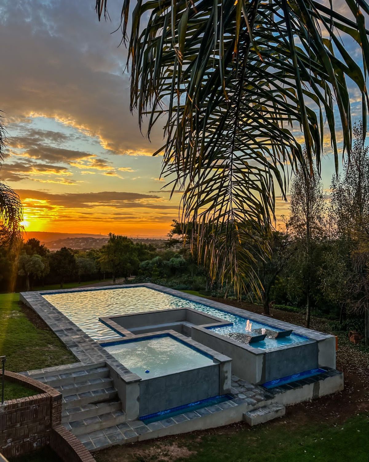 Raised pool and spa at sunset beneath a palm, overlooking a valley