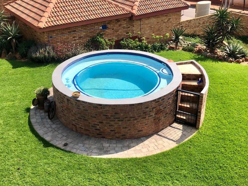 Round raised brick pool with steps on a green lawn