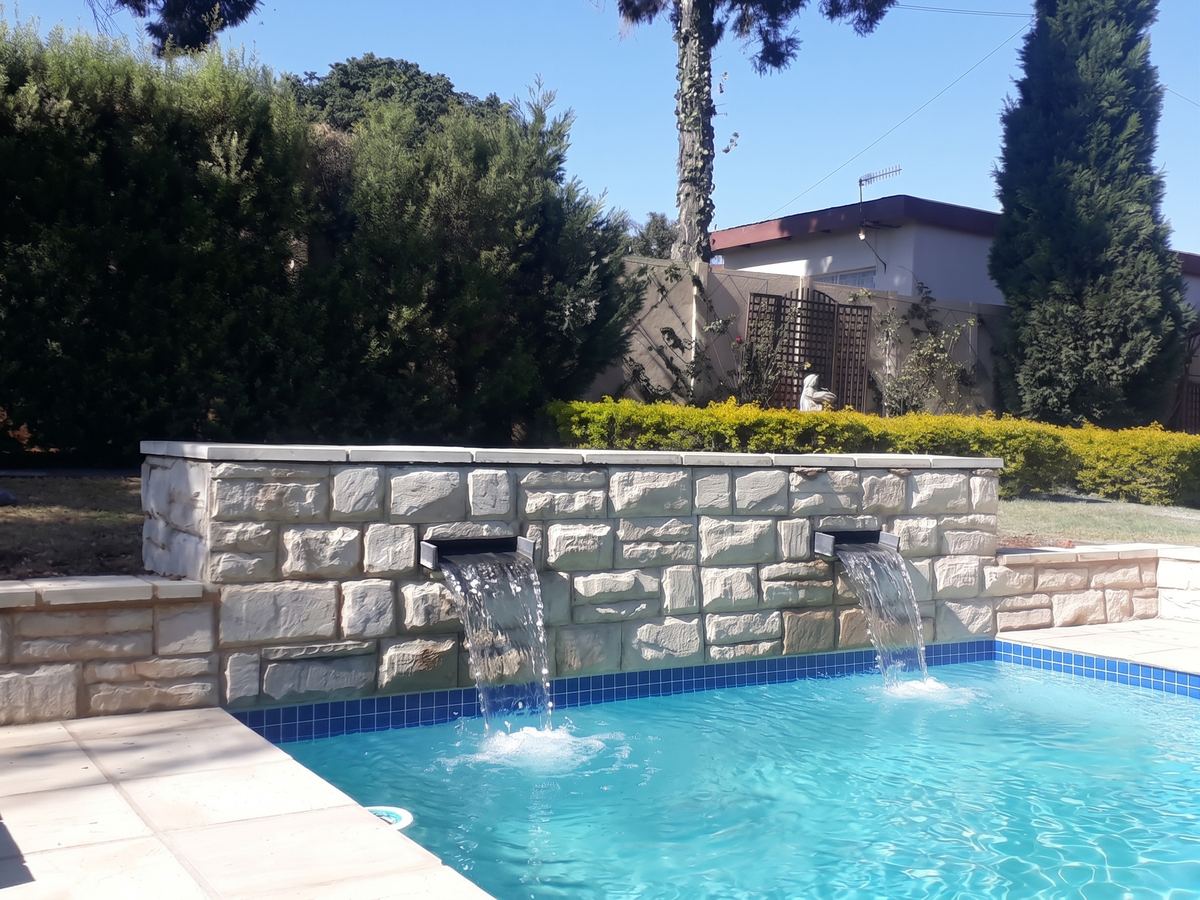 Stone wall water feature spilling into a pool