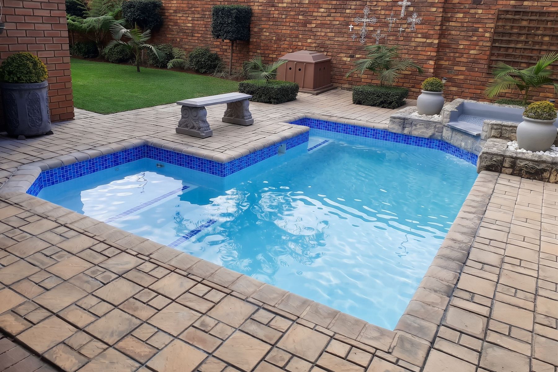 L-shaped pool with blue mosaic band and stone bench